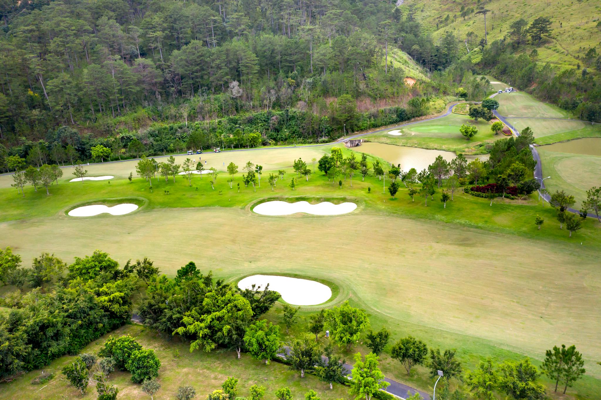 Aerial shot of a lush green golf course surrounded by nature and hills.