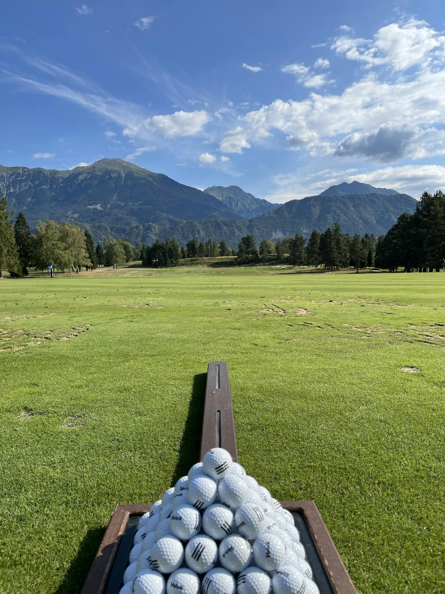 Golf balls ready for play on a scenic course in Jesenice, Slovenia, surrounded by mountains.